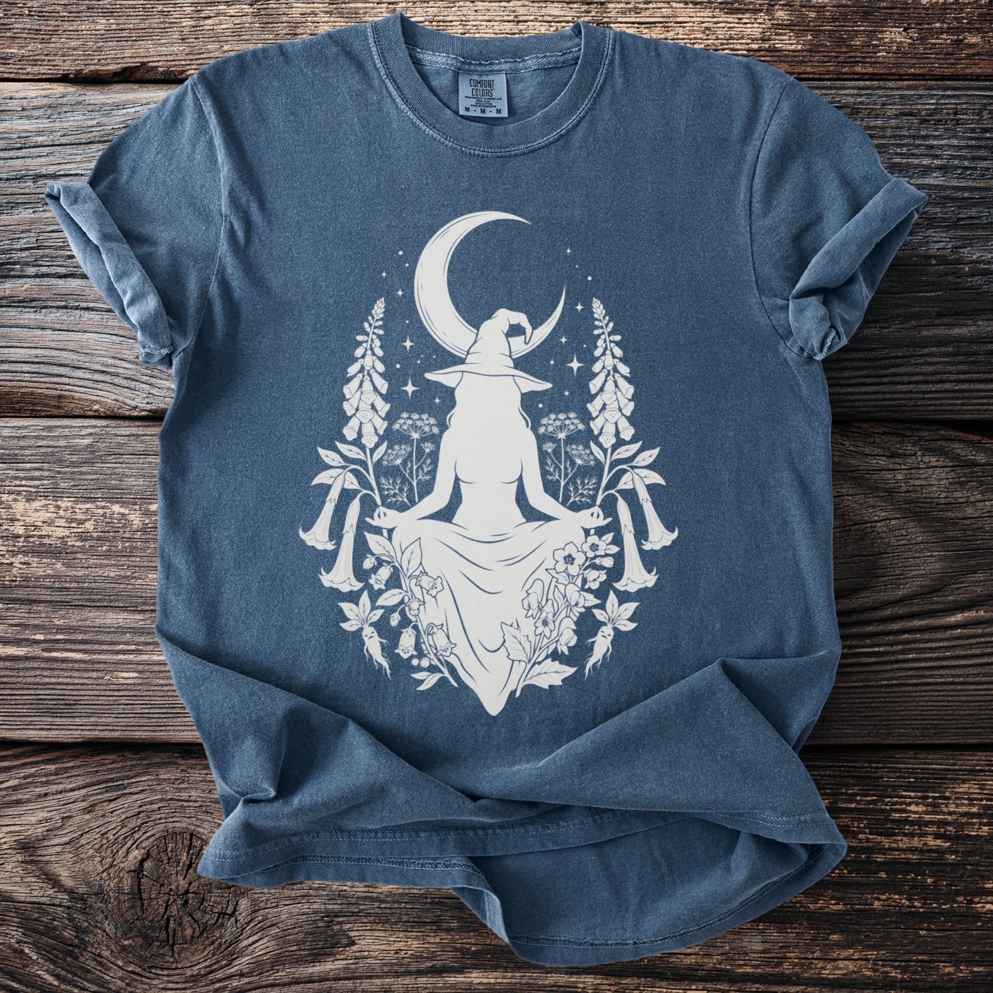 Blue t-shirt with white witch, moon, stars, and botanical graphic.
