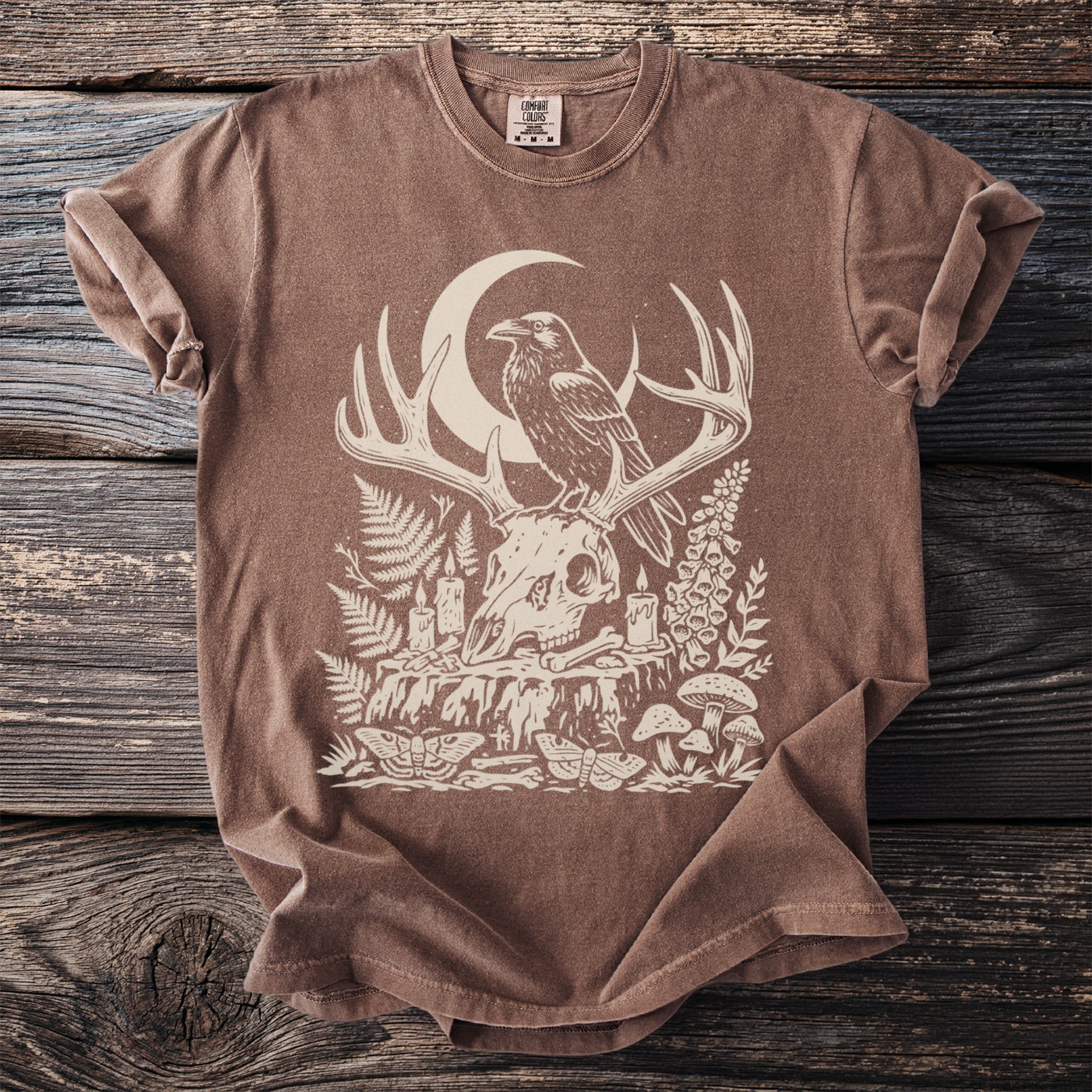 Brown t-shirt with a raven on antlers, moon, skull, and woodland elements.