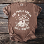 Brown t-shirt with white text and graphic of frog and mushroom saying "God forbid women have hobbies".
