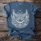 Blue t-shirt with white moth, crescent moon, candles, and floral graphic.