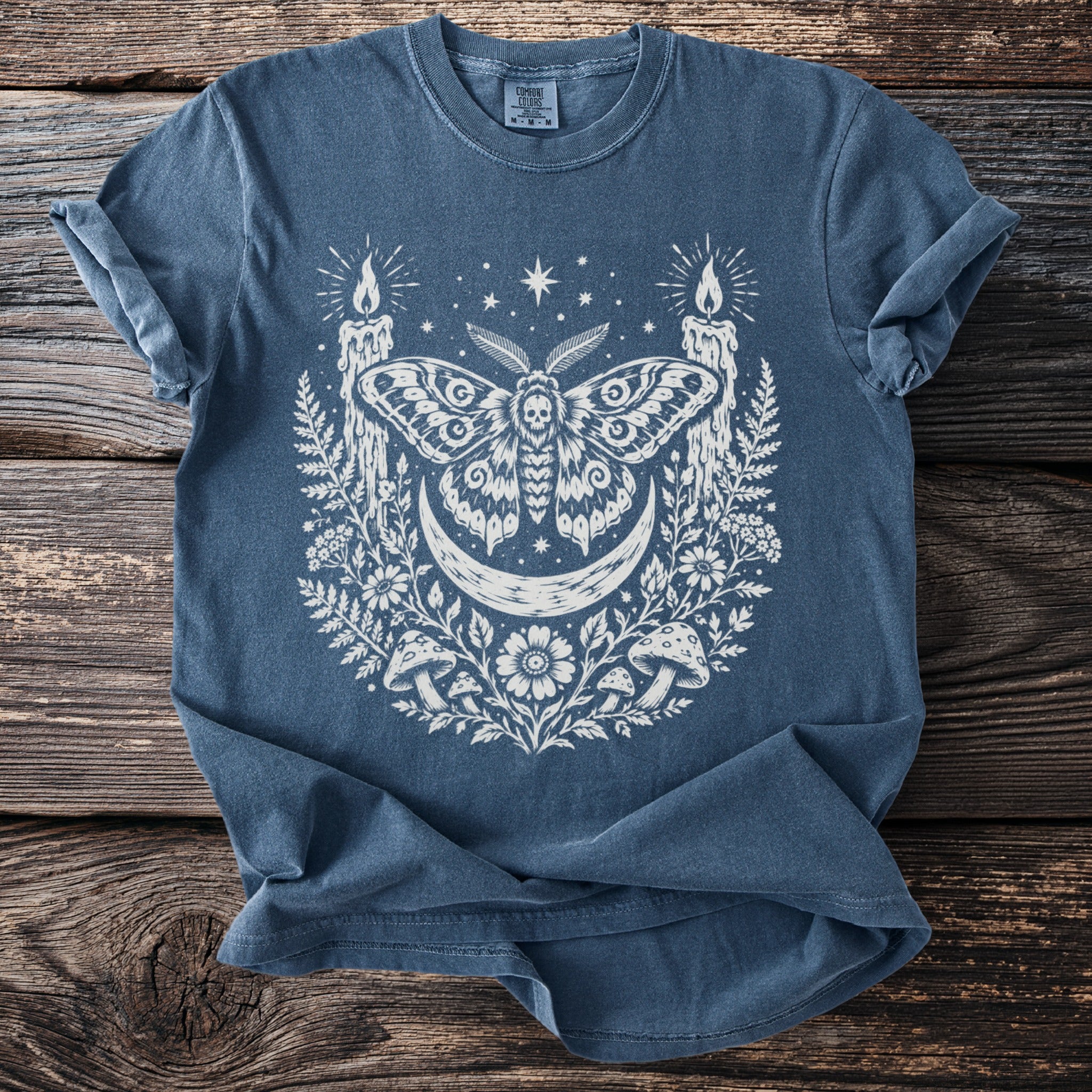 Blue t-shirt with white moth, crescent moon, candles, and floral graphic.