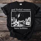Black t-shirt with text "god forbid women have hobbies" and a dark illustration.