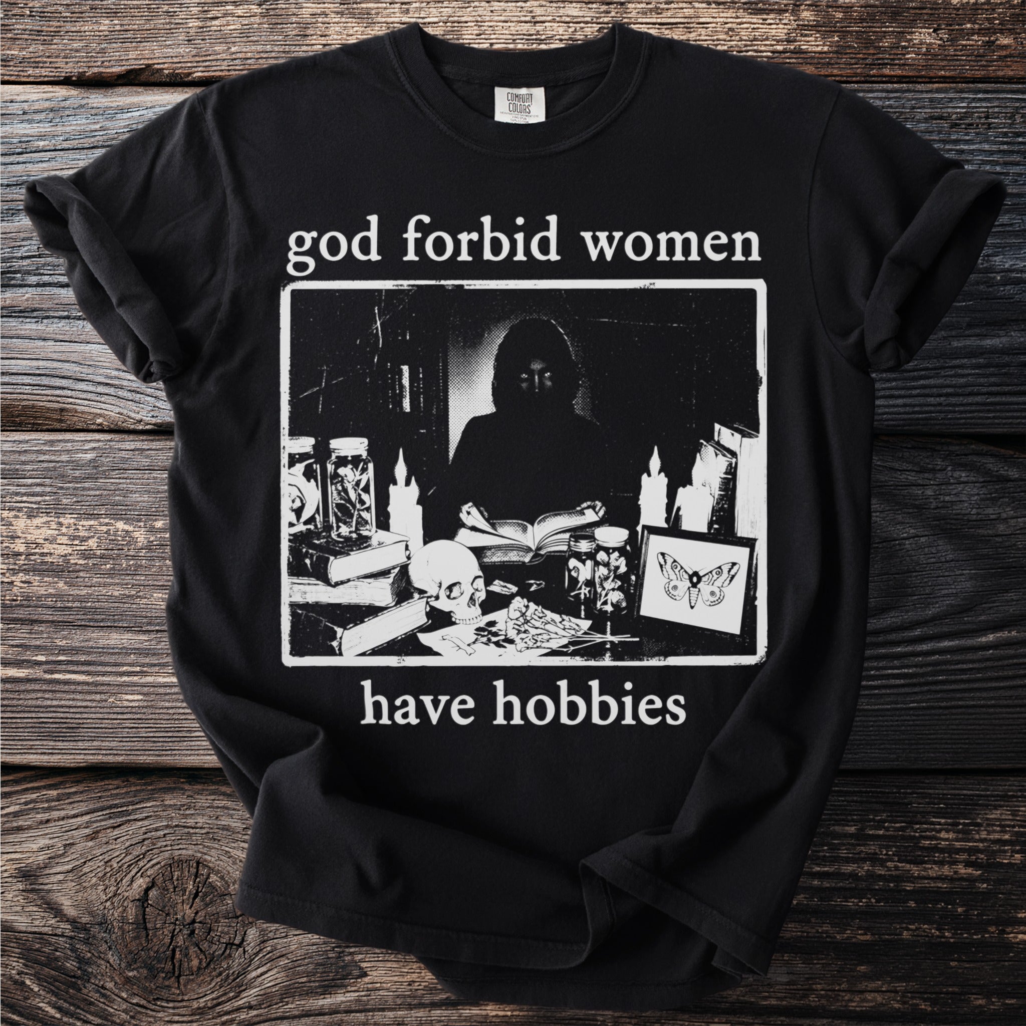 Black t-shirt with text "god forbid women have hobbies" and a dark illustration.