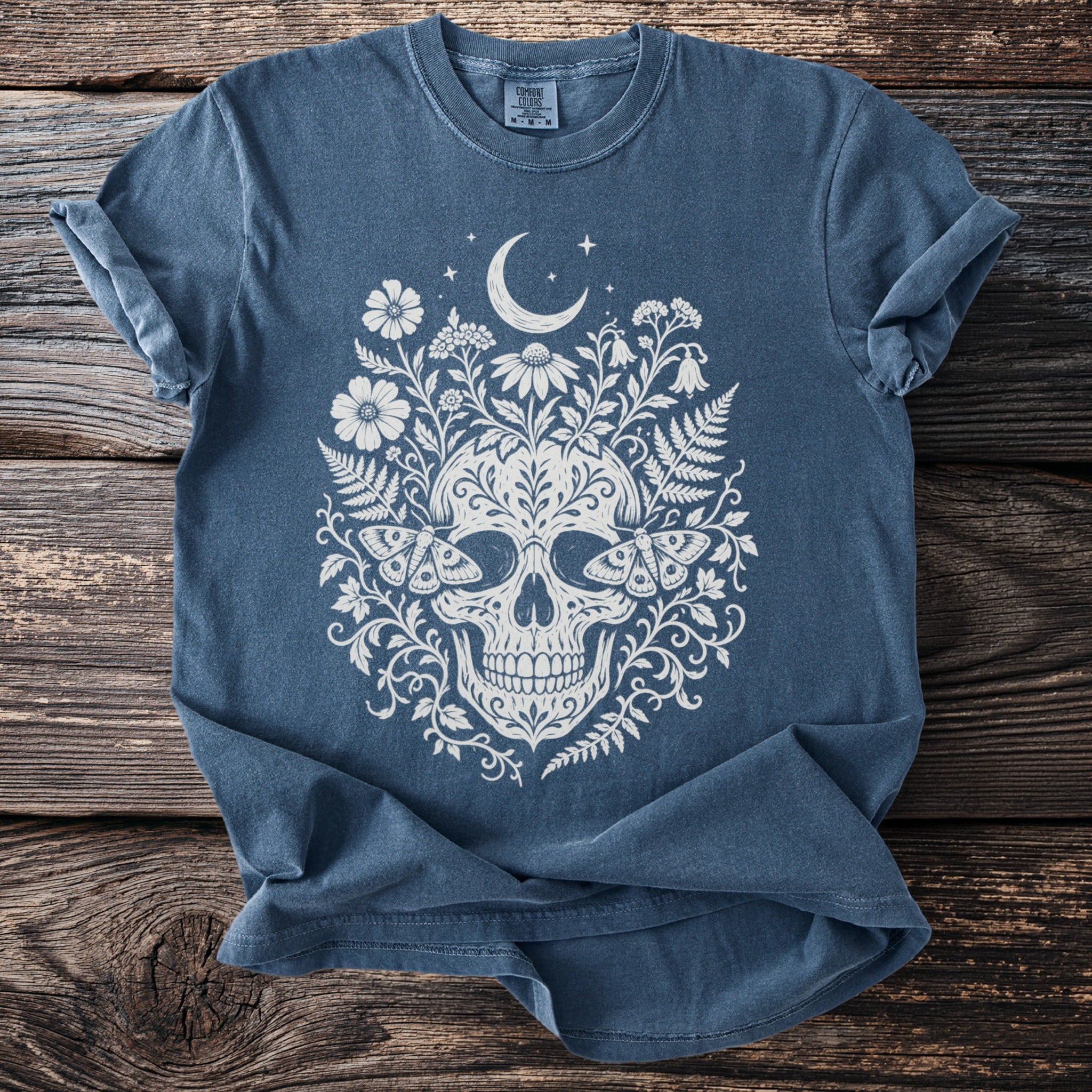 Blue t-shirt with cream skull, floral, moon, and moth graphic.