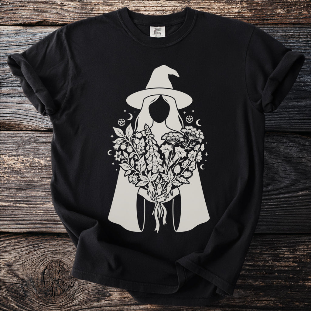 Black t-shirt with a light gray graphic of a witch holding botanical elements.