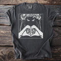 Graphic t-shirt with woman's eyes, floral crown, and hands forming heart around pomegranate.