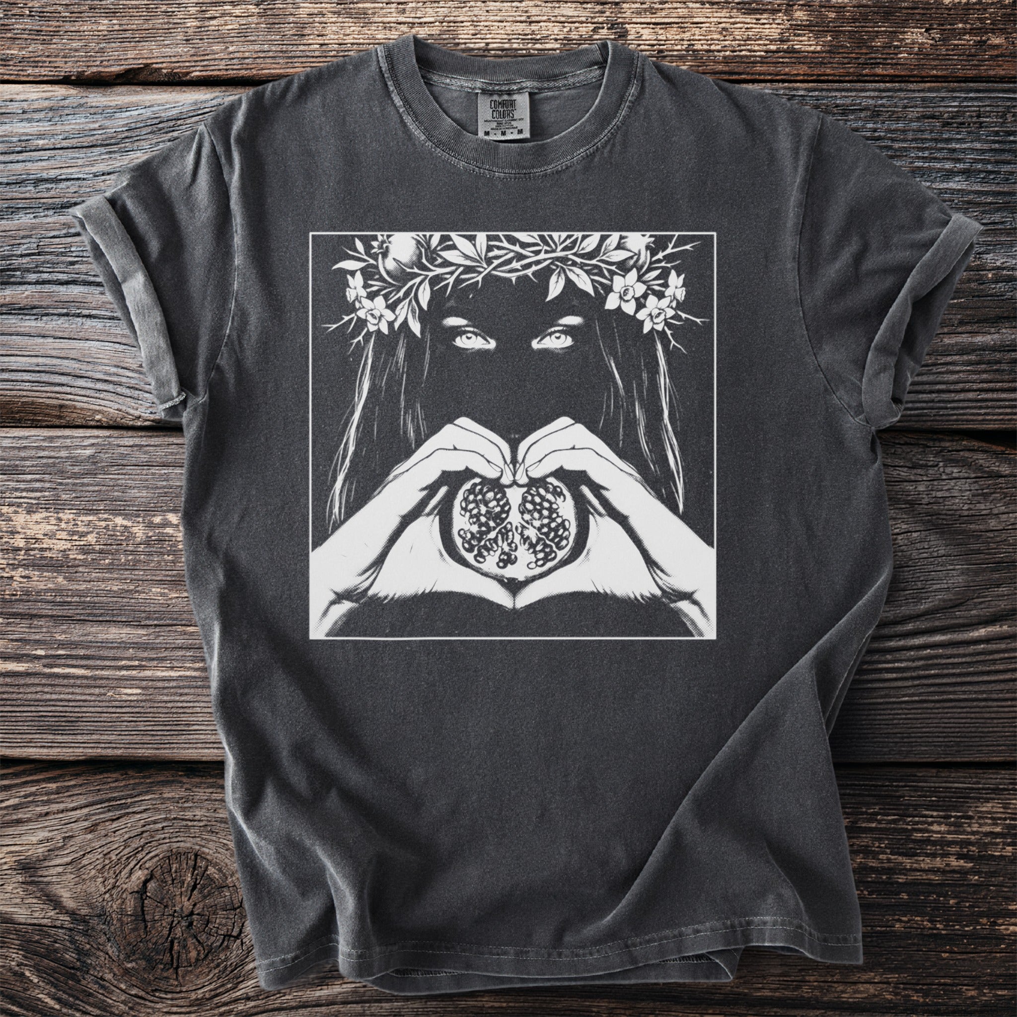 Graphic t-shirt with woman's eyes, floral crown, and hands forming heart around pomegranate.