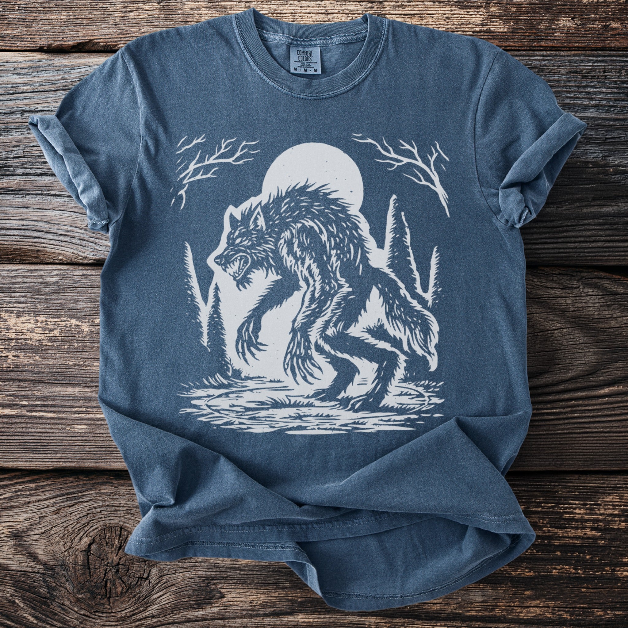 Blue t-shirt with a white graphic of a werewolf in a forest under a full moon.