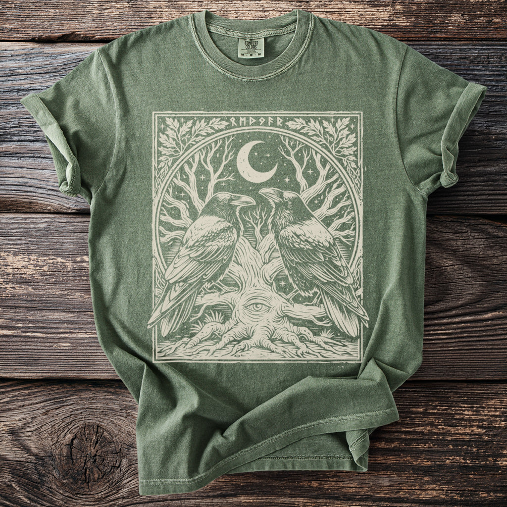 Green t-shirt with a linocut design of two ravens, a moon, and a tree with an eye.