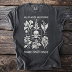 Dark t-shirt with skull and crossbones surrounded by botanical illustrations and the text "ALL PLANTS ARE EDIBLE SOME ONLY ONCE."