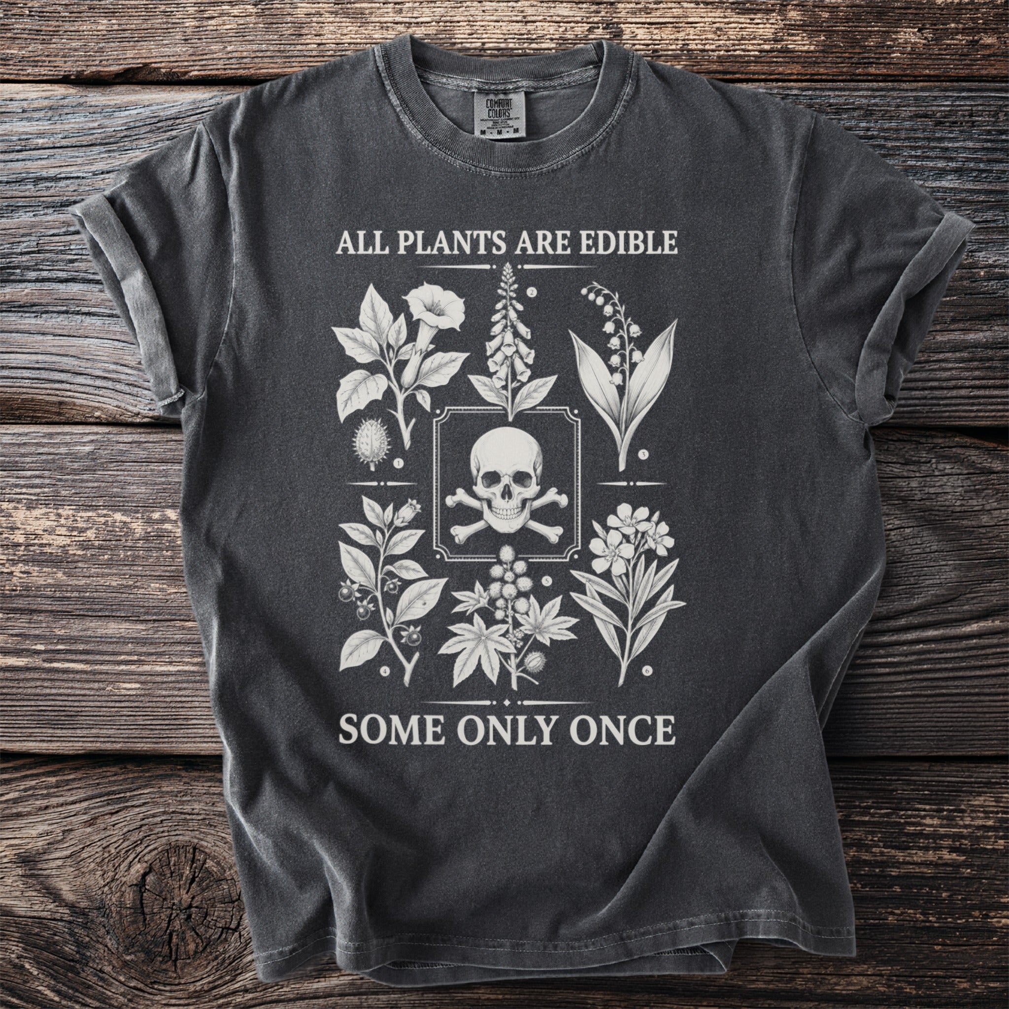 Dark t-shirt with skull and crossbones surrounded by botanical illustrations and the text "ALL PLANTS ARE EDIBLE SOME ONLY ONCE."