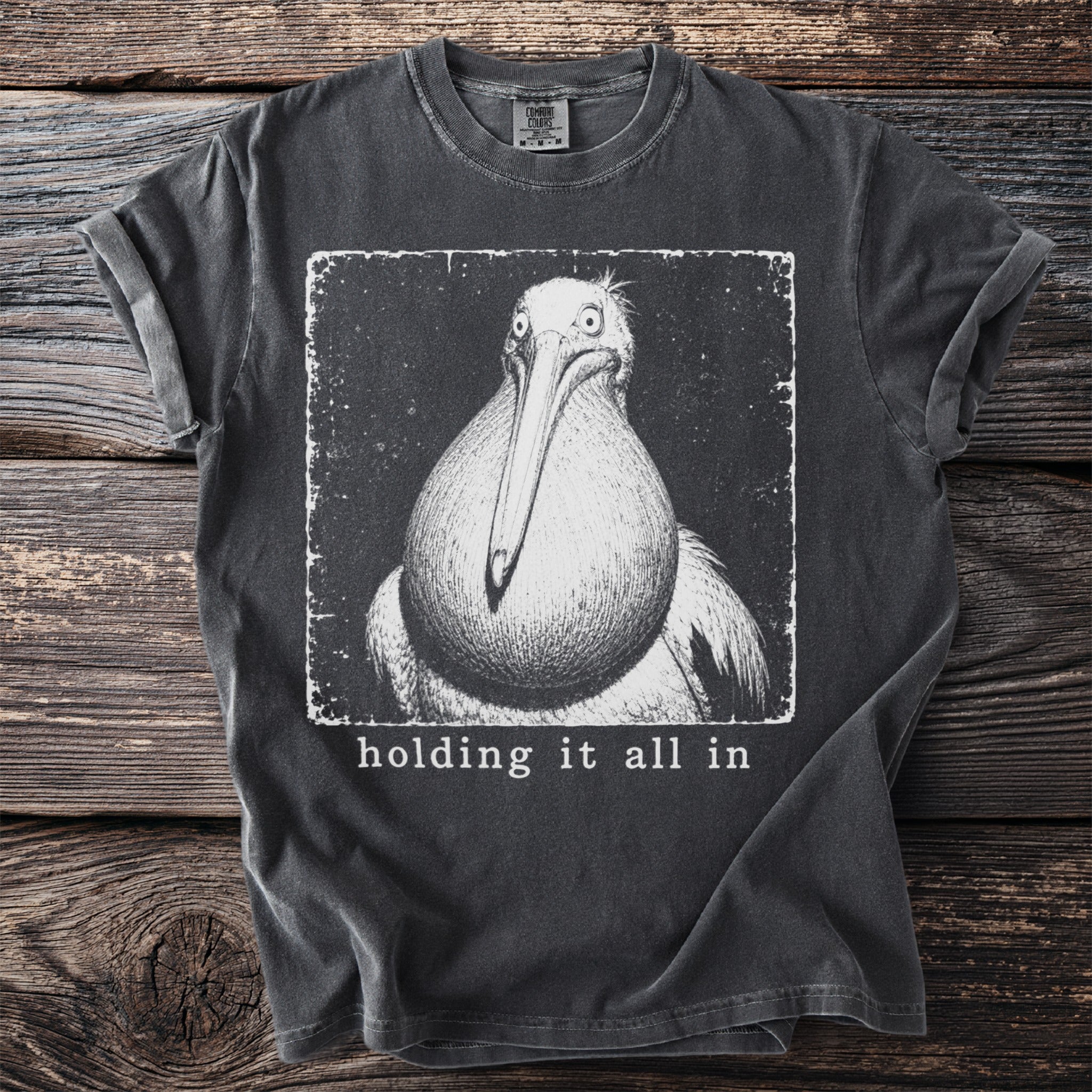 Dark grey t-shirt with a black and white drawing of a pelican and the text "holding it all in".