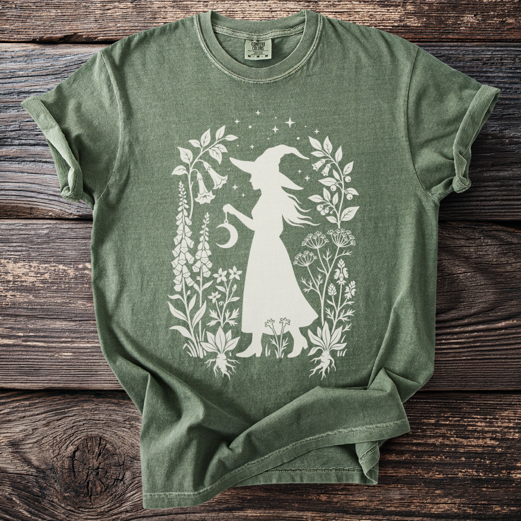 Green t-shirt with white silhouette of a witch and celestial botanical floral design.