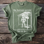 Green t-shirt with text "the horrors persist but so do i" and wolf graphic.