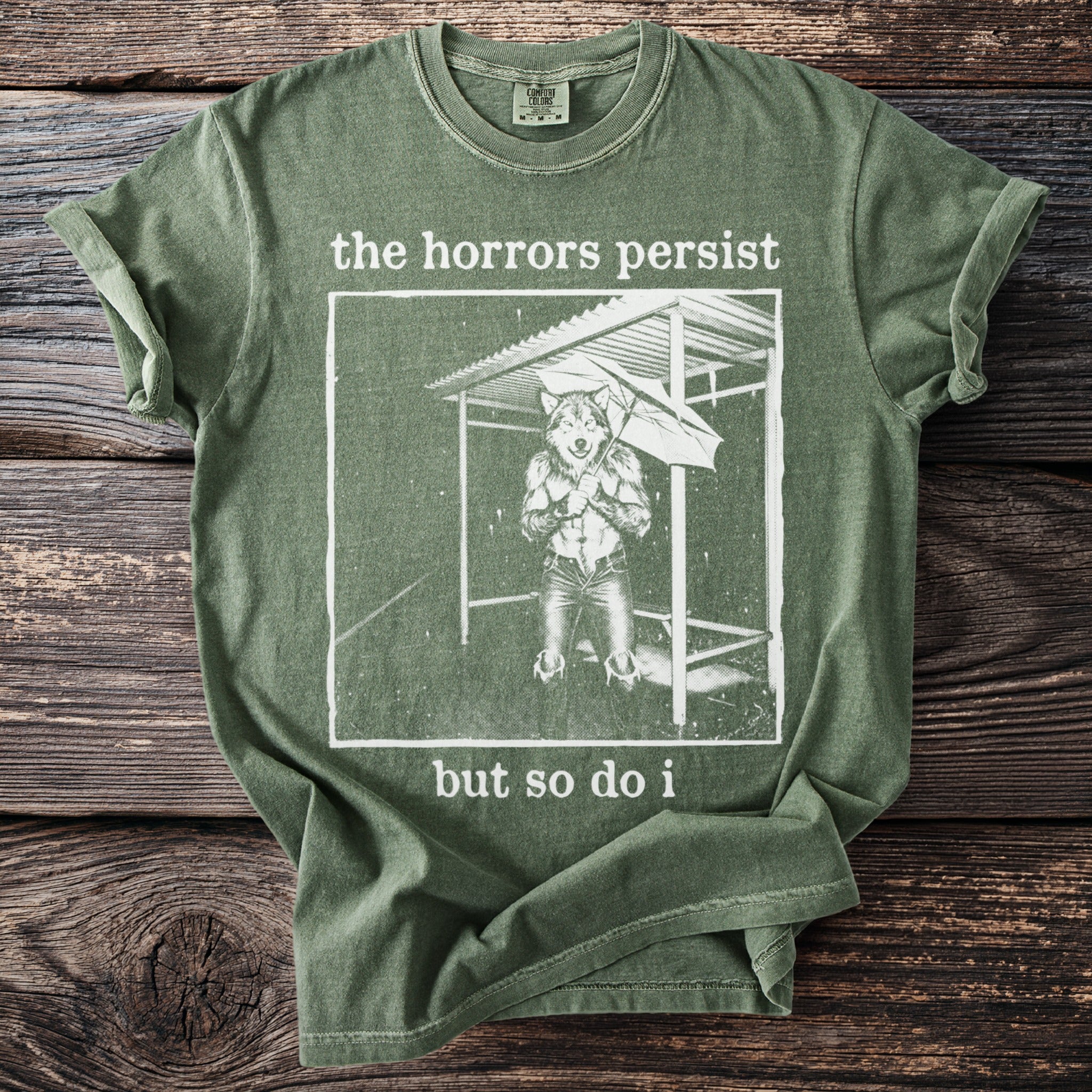 Green t-shirt with text "the horrors persist but so do i" and wolf graphic.