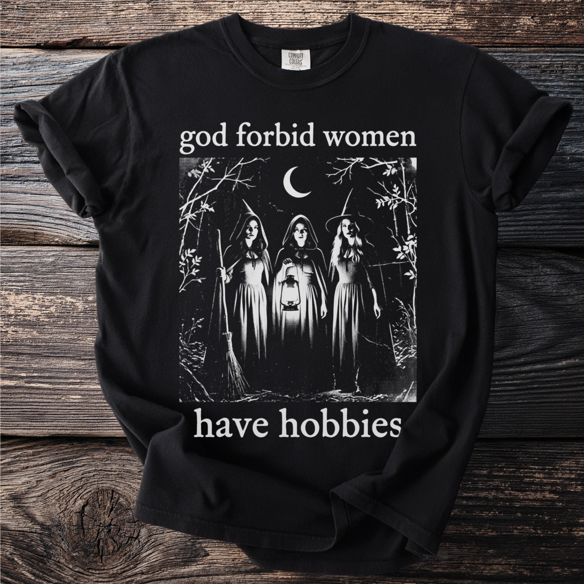 Black t-shirt with "god forbid women have hobbies" and a witch illustration.