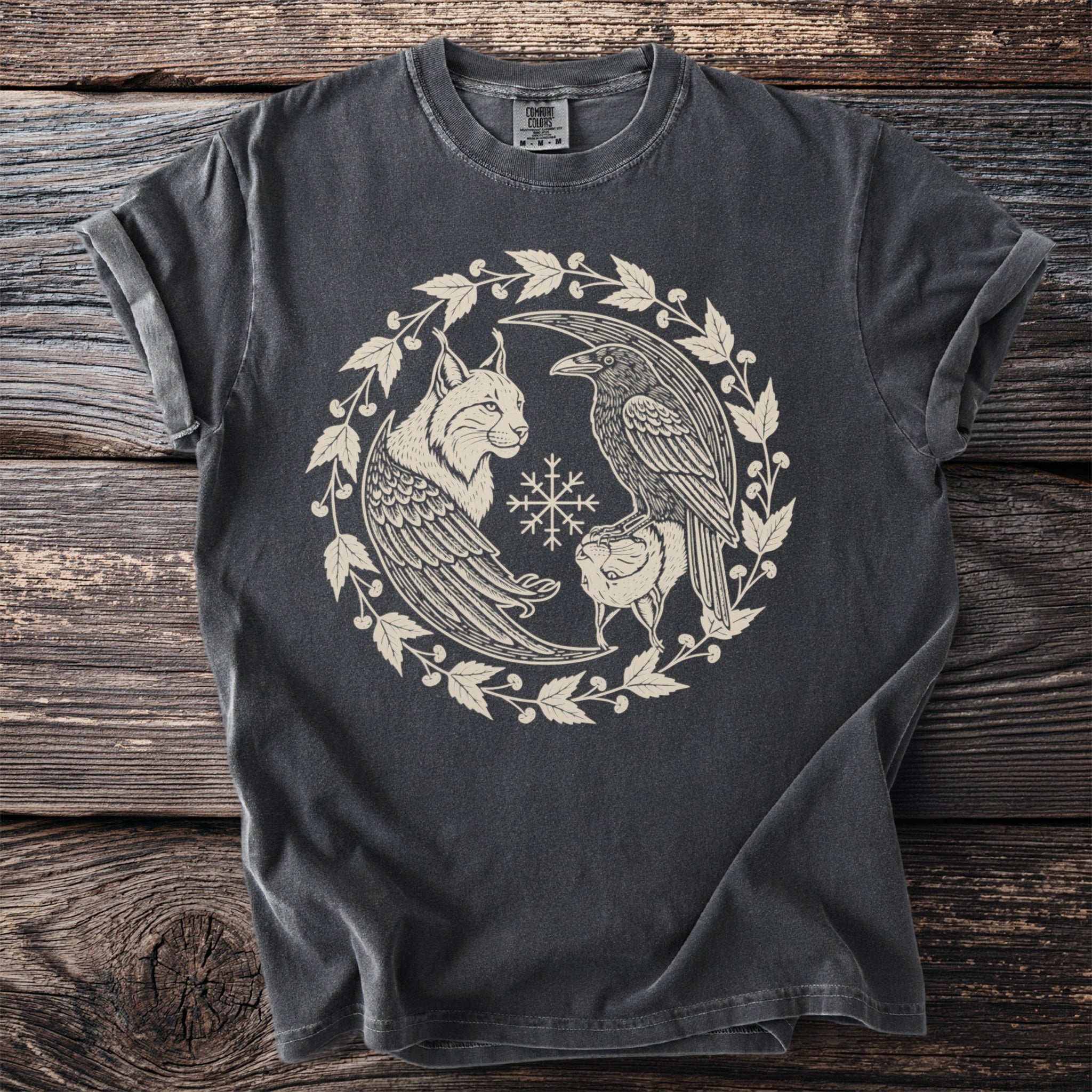 Dark grey t-shirt with cream lynx, raven, and snowflake design within a leafy circle.