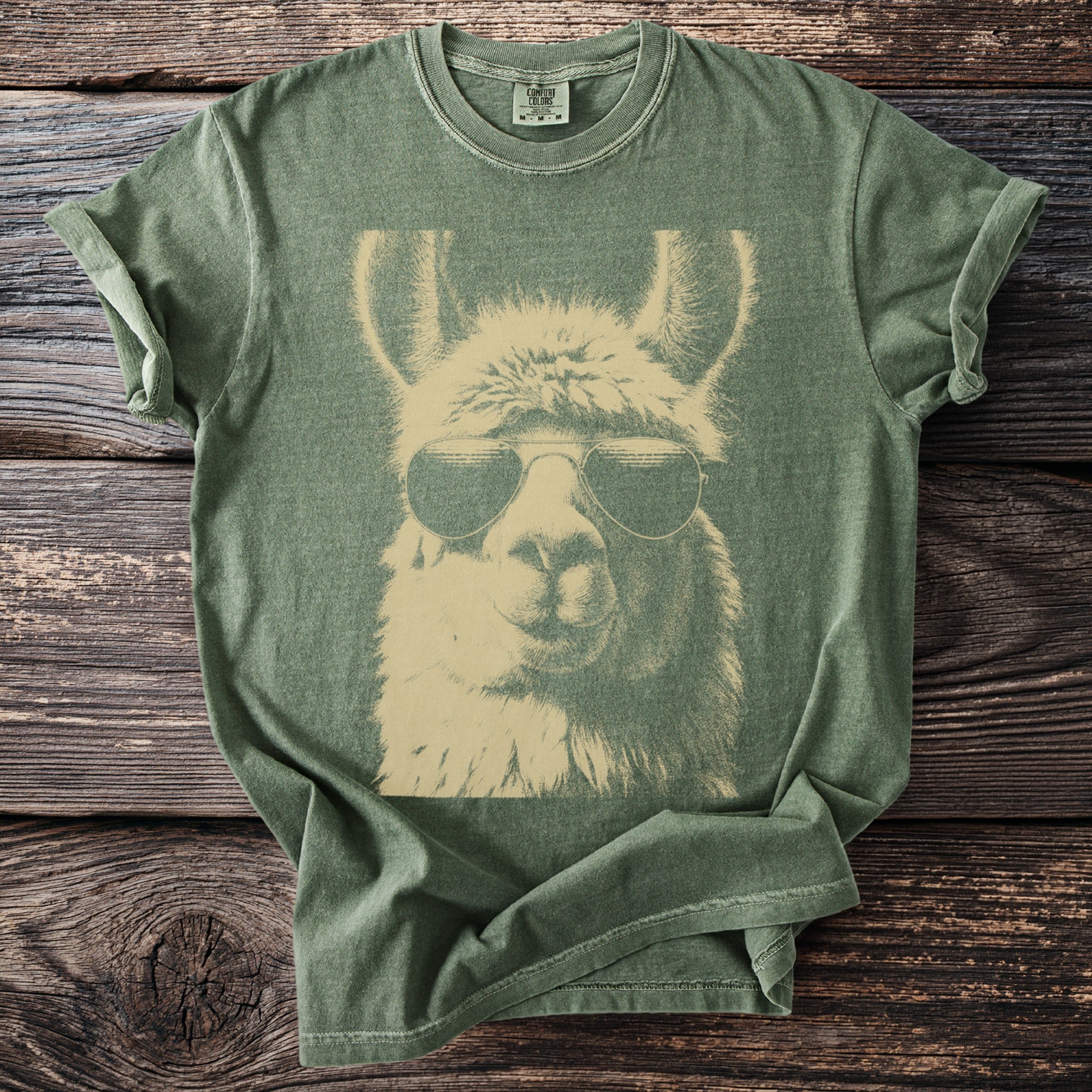 Green t-shirt with a beige graphic of a llama wearing aviator sunglasses.
