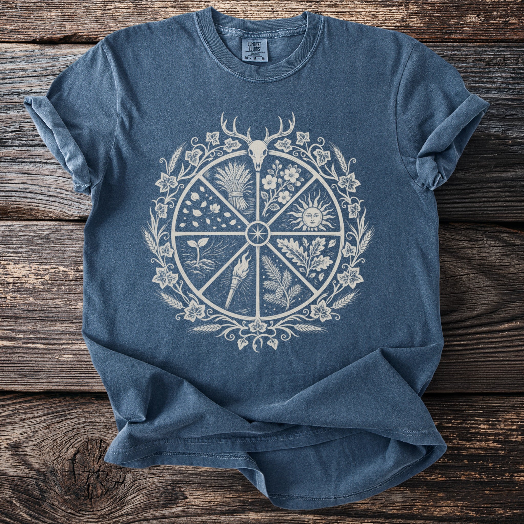 Blue t-shirt with a circular design featuring a deer skull, sun, plants, and a torch.