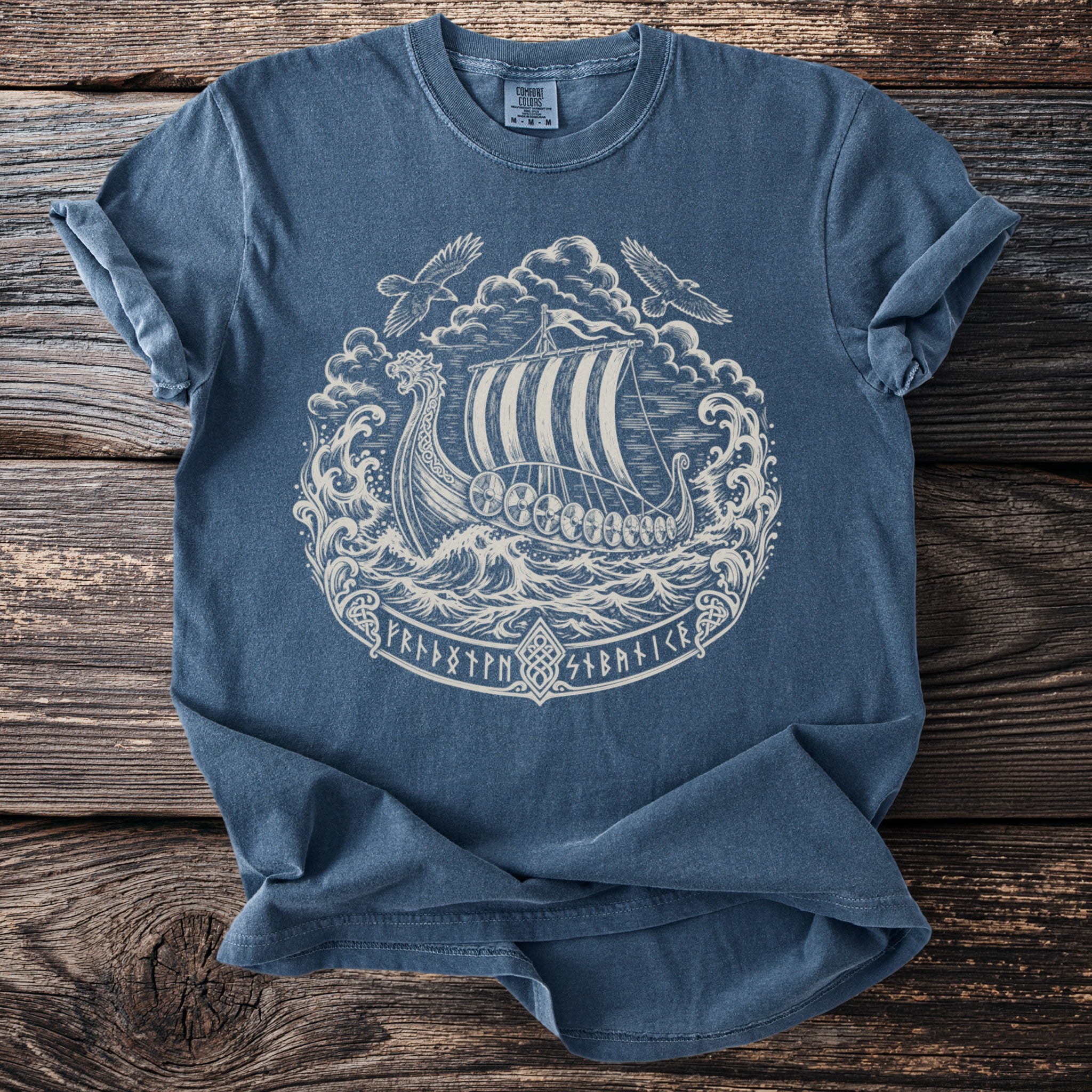 Blue t-shirt with a white print of a Viking ship, waves, dragons, eagles, and runes.