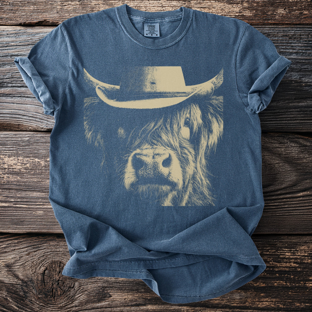 Blue t-shirt with a cream line drawing of a Highland cow wearing a cowboy hat.