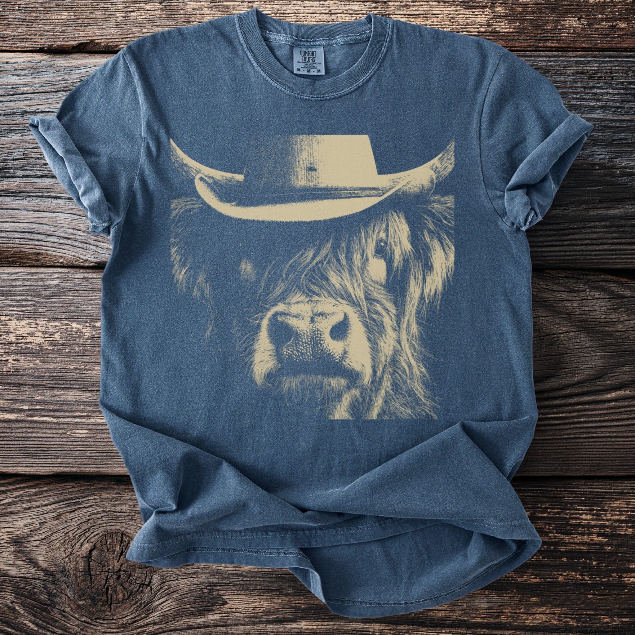 Blue t-shirt with a cream line drawing of a Highland cow wearing a cowboy hat.