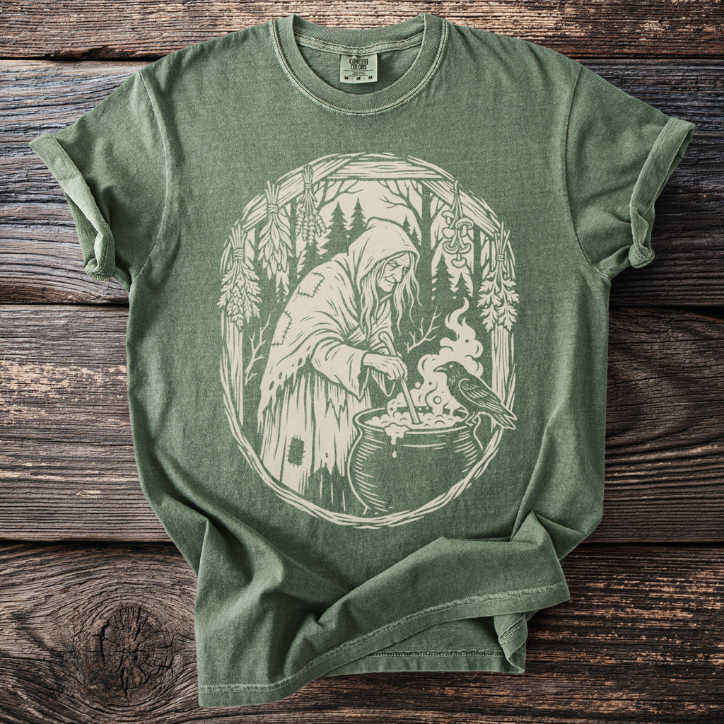 Green t-shirt with a white graphic of a witch brewing a potion with a raven.