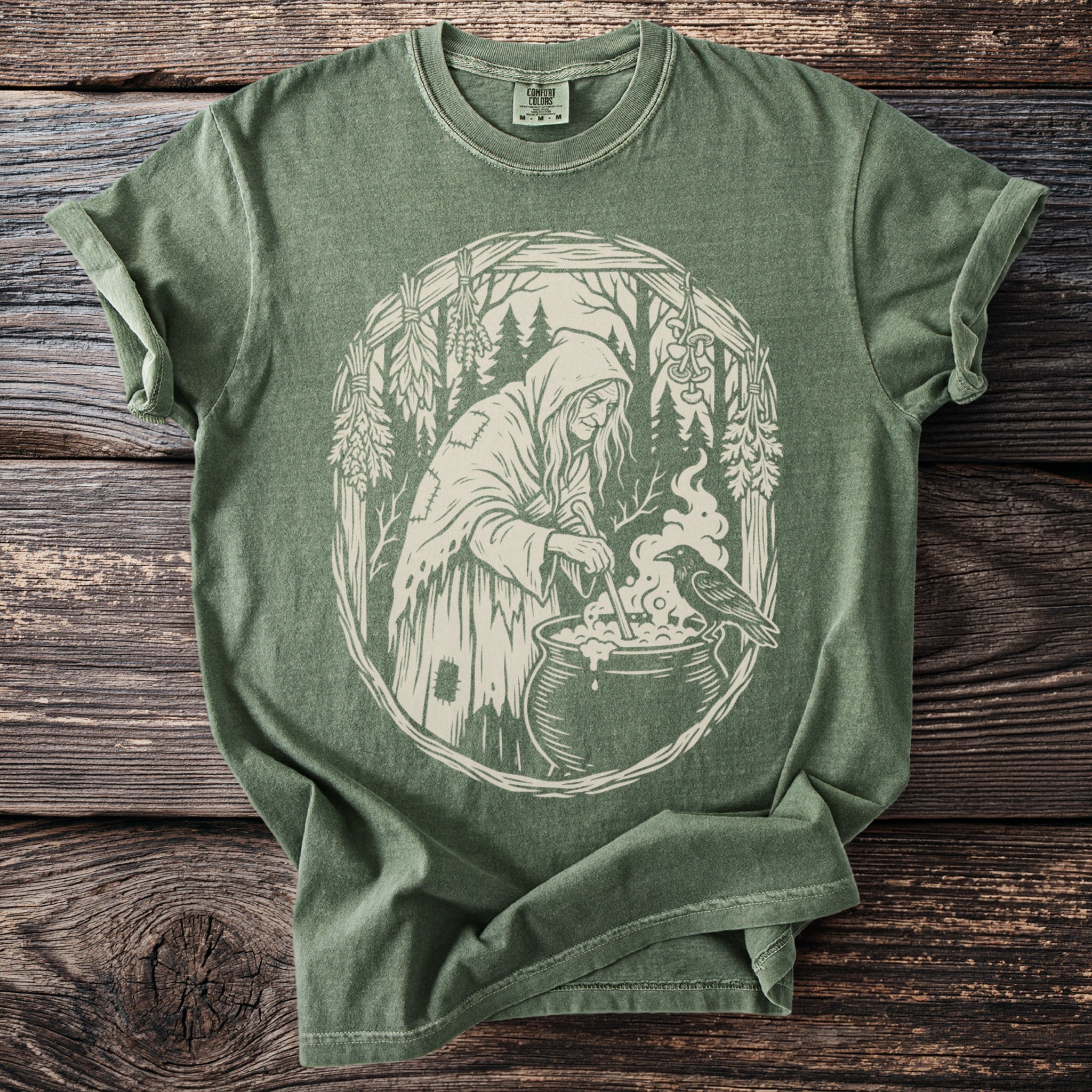 Green t-shirt with a white graphic of a witch brewing a potion with a raven.