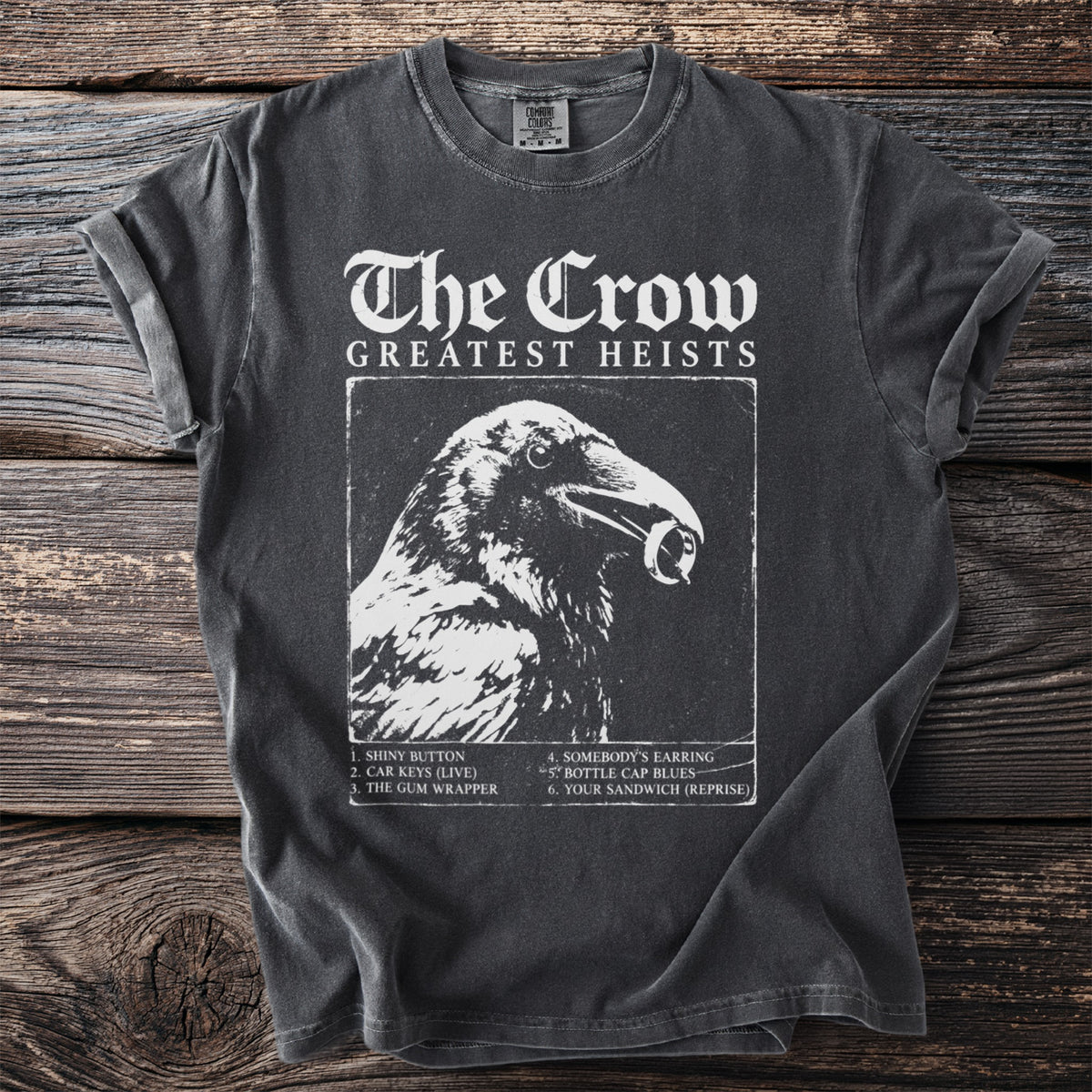 Dark grey t-shirt with "The Crow Greatest Heists" and a crow holding a ring.