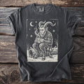 Pepper gray t-shirt with a cream folk-cut print: Krampus sits on a fallen log in the snow, both hands around a steaming mug.