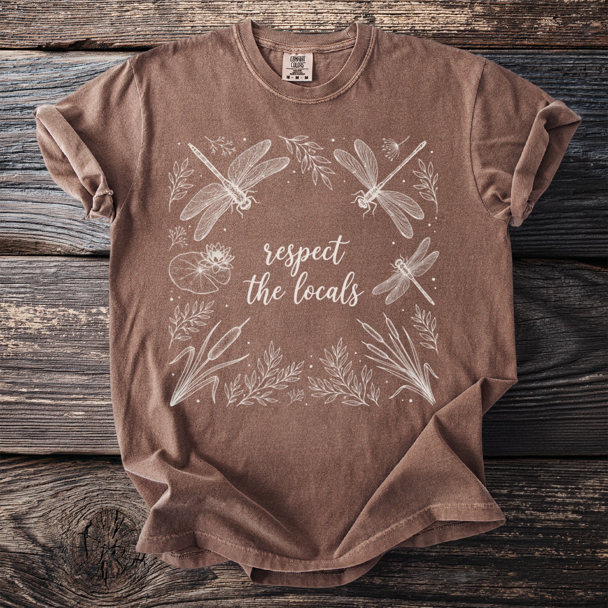 Brown t-shirt with white dragonfly and floral design; text says "respect the locals".