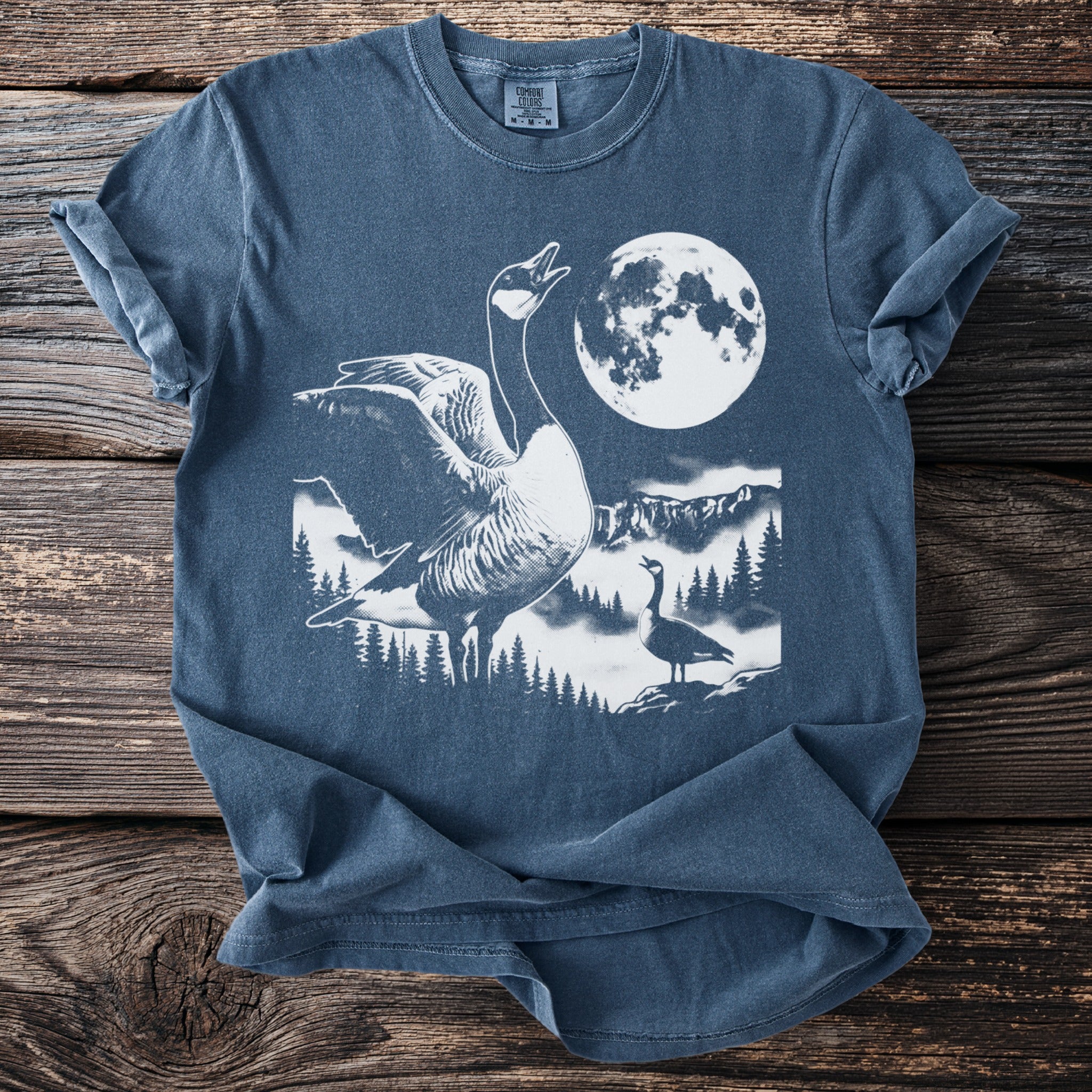 Blue t-shirt with graphic of geese in a forest under a full moon.
