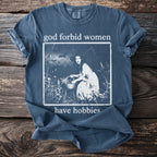 Blue t-shirt with text "god forbid women have hobbies" and a vintage illustration.