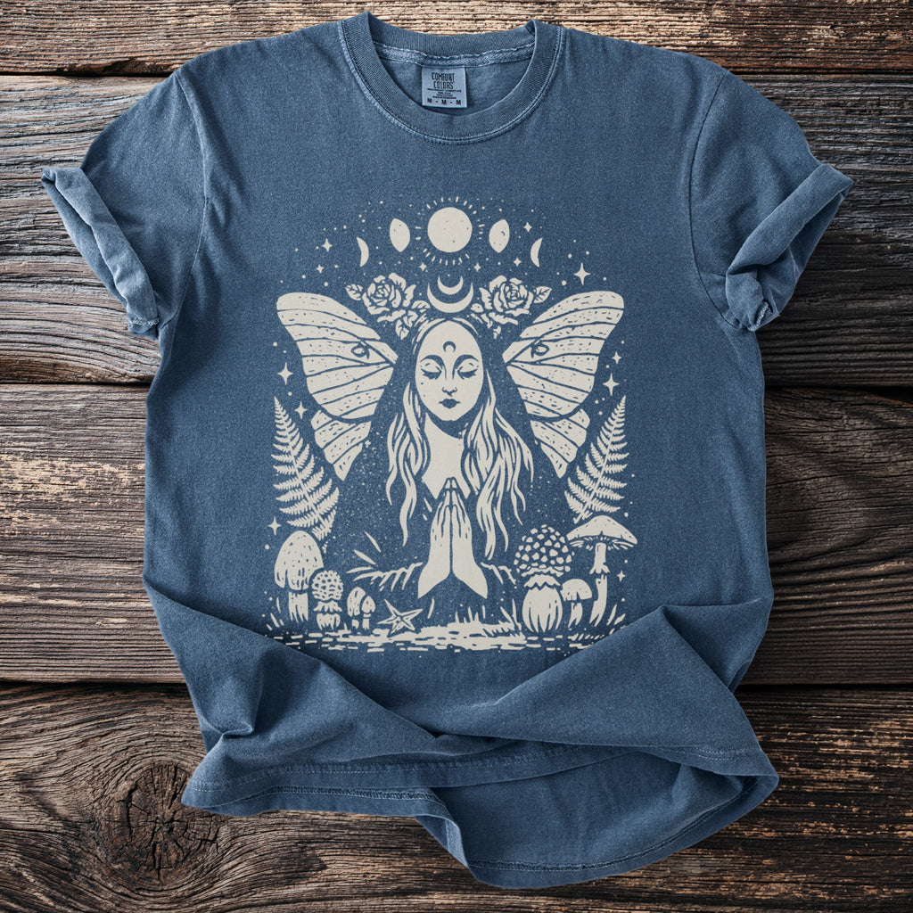 Blue t-shirt with cream print of a woman praying with moth wings and celestial elements.