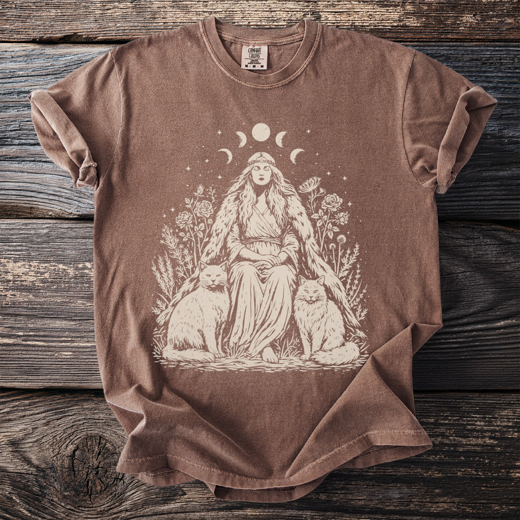 Brown t-shirt with cream graphic of a woman, two cats, moon phases, and celestial accents.