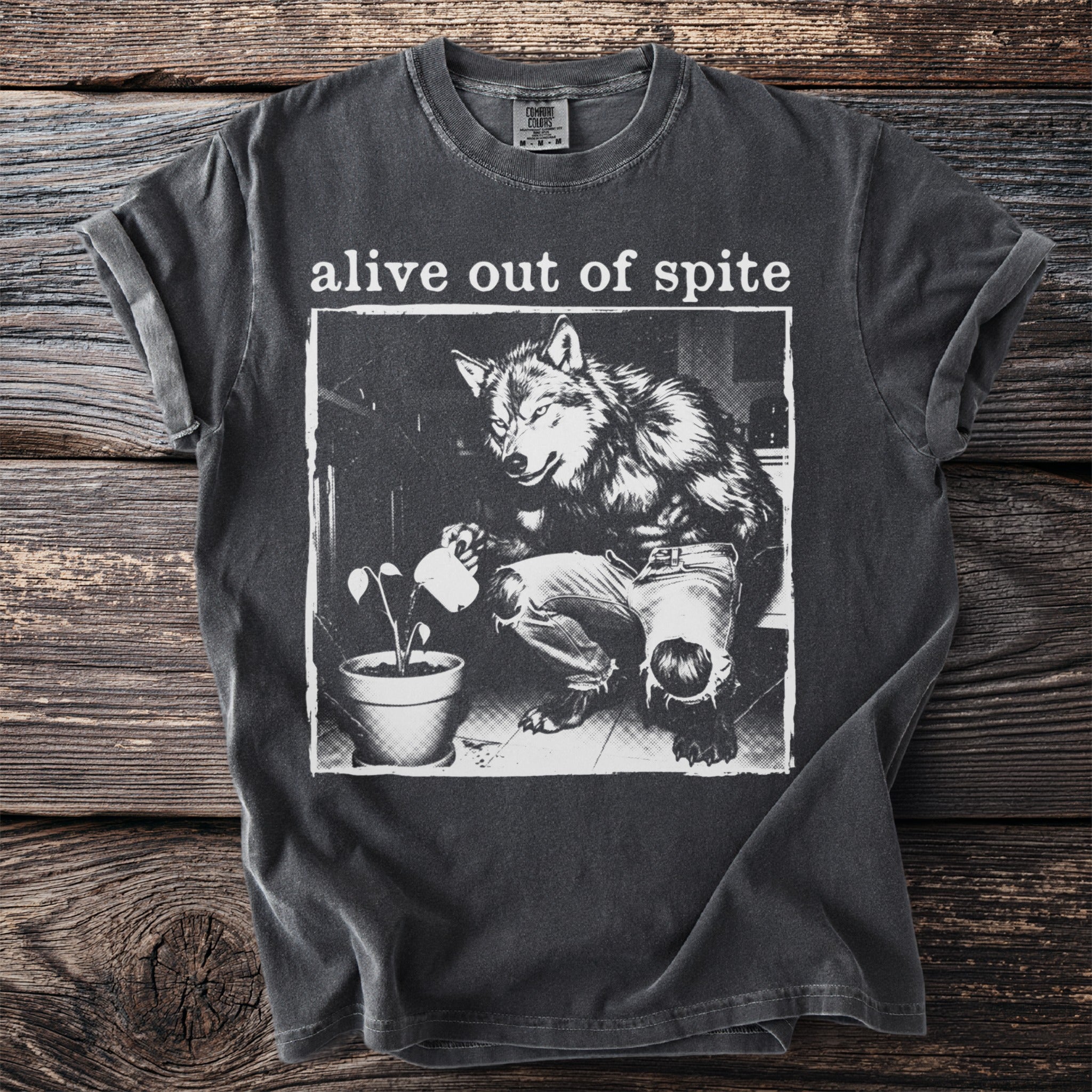 Dark gray t-shirt with "alive out of spite" and wolf watering a plant graphic.