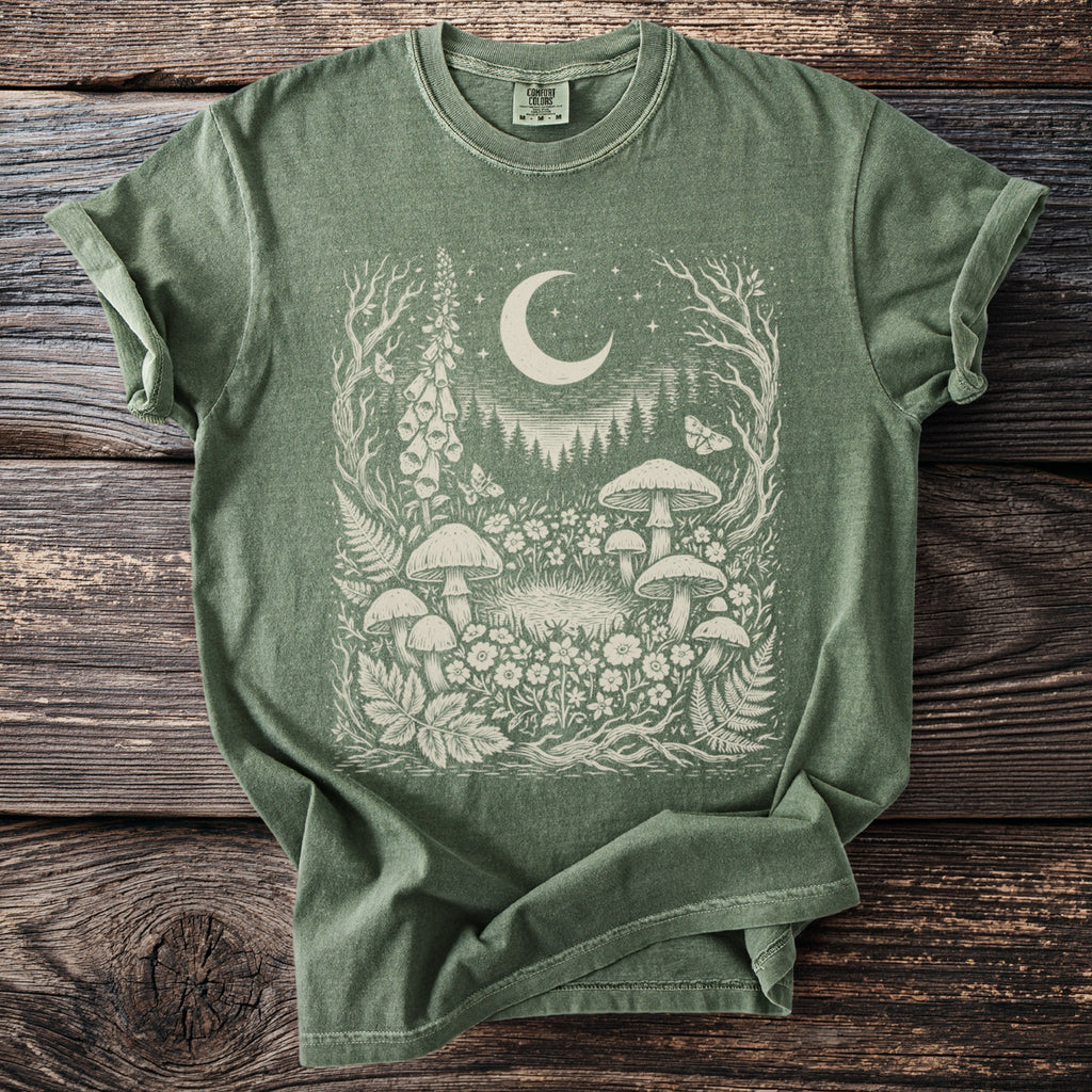 Green t-shirt with a cream graphic of mushrooms, flowers, butterflies, and a crescent moon.