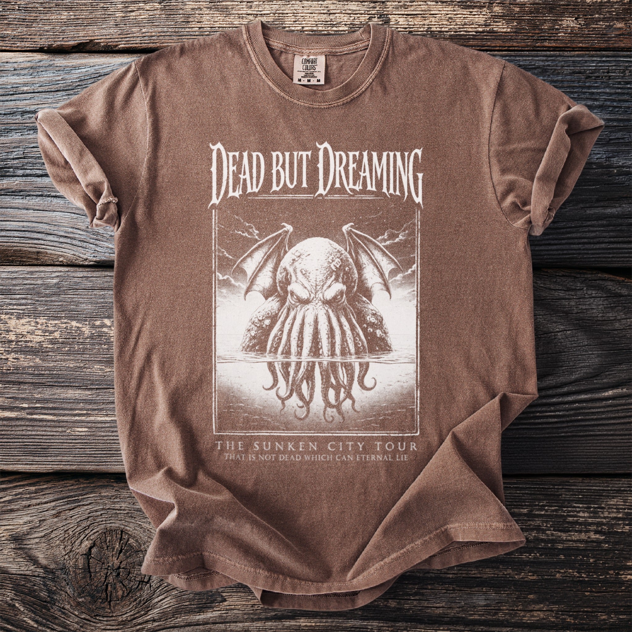 Brown t-shirt with "Dead But Dreaming" and tentacled creature graphic, "The Sunken City Tour" text.