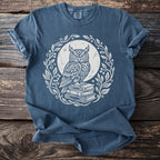 Blue t-shirt with white owl graphic sitting on books, surrounded by leaves.