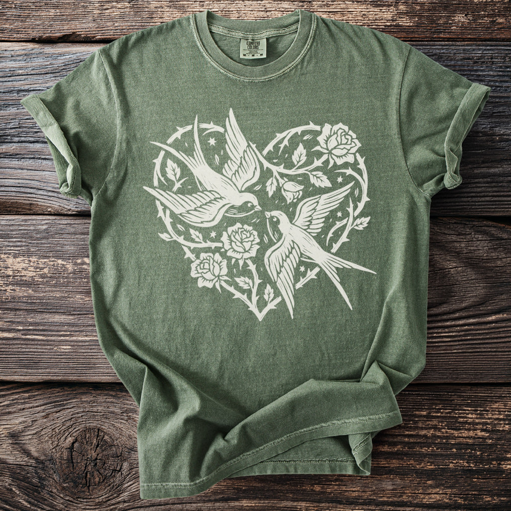 Green t-shirt with white print of two swallows and roses in a heart shape.