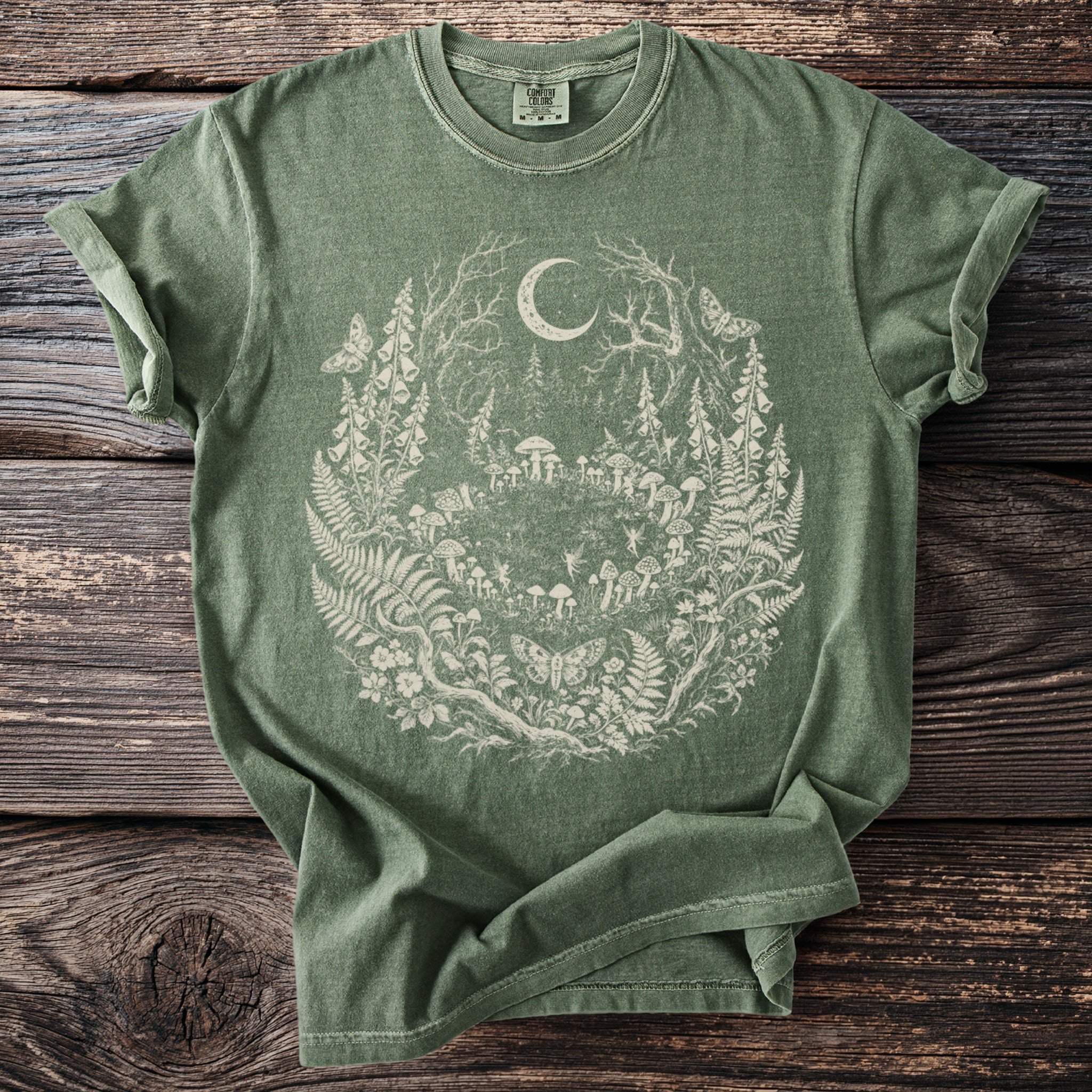 Green t-shirt with a delicate line art design of a magical forest scene and crescent moon.