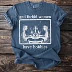 Dark blue t-shirt with white graphic of three women around a Ouija board and text "god forbid women have hobbies".