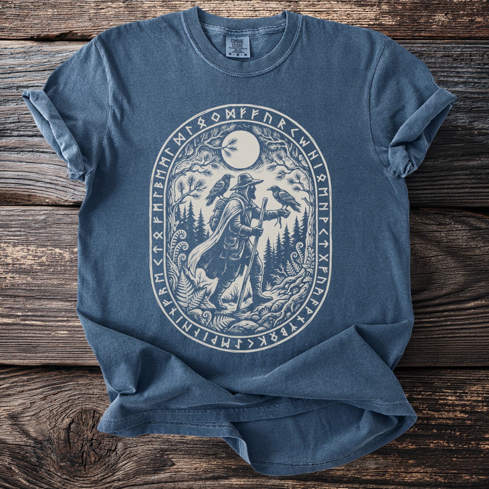 Blue t-shirt with oval graphic of hiker, ravens, moon, and runes.