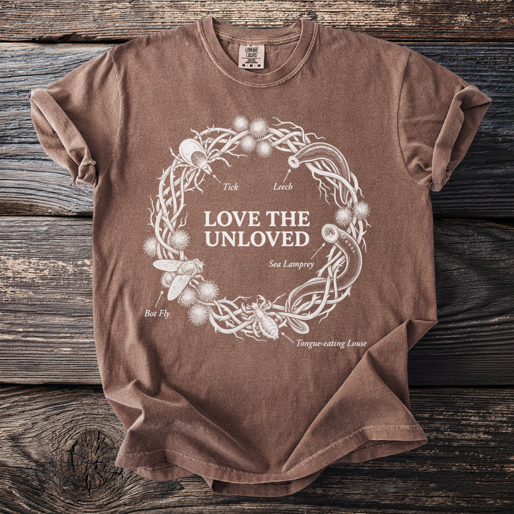 Brown t-shirt with "LOVE THE UNLOVED" and a botanical-style illustration of misunderstood creatures.