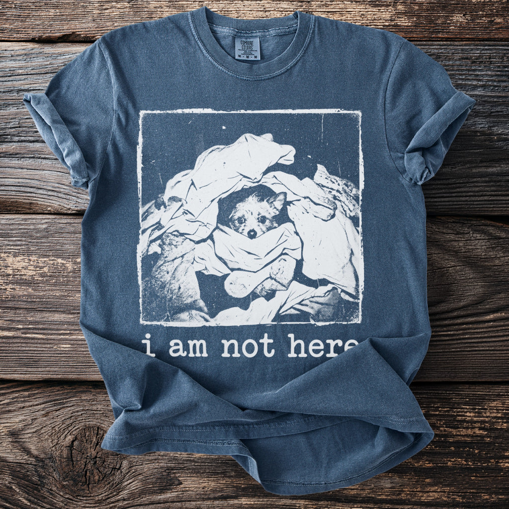 Blue t-shirt with a dog peeking out of laundry and the text "i am not here."
