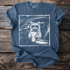 Graphic tee with a raccoon in sunglasses holding a drink inside a car.
