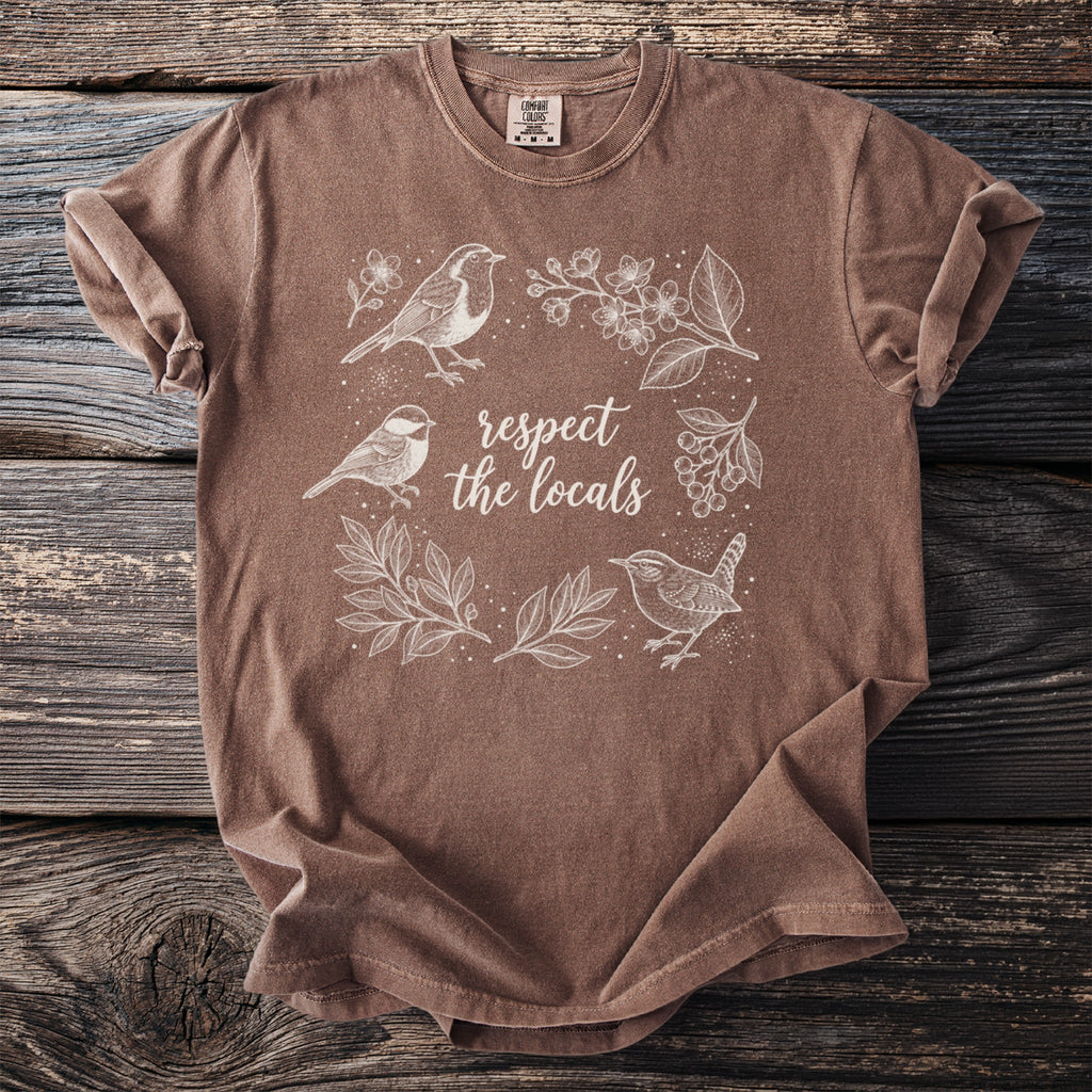 Brown t-shirt with white line art of birds and plants, reading "respect the locals".