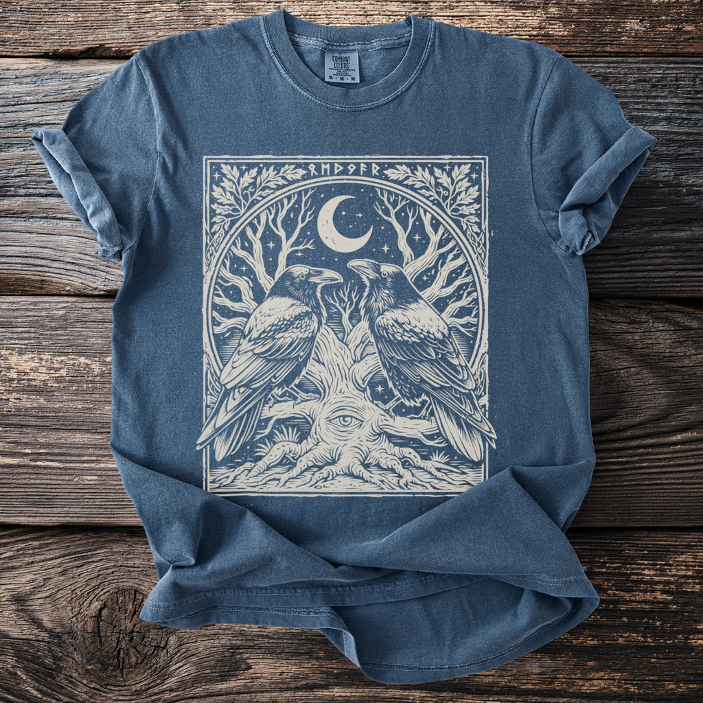 Blue t-shirt with a graphic of two ravens on a tree with an eye and moon.