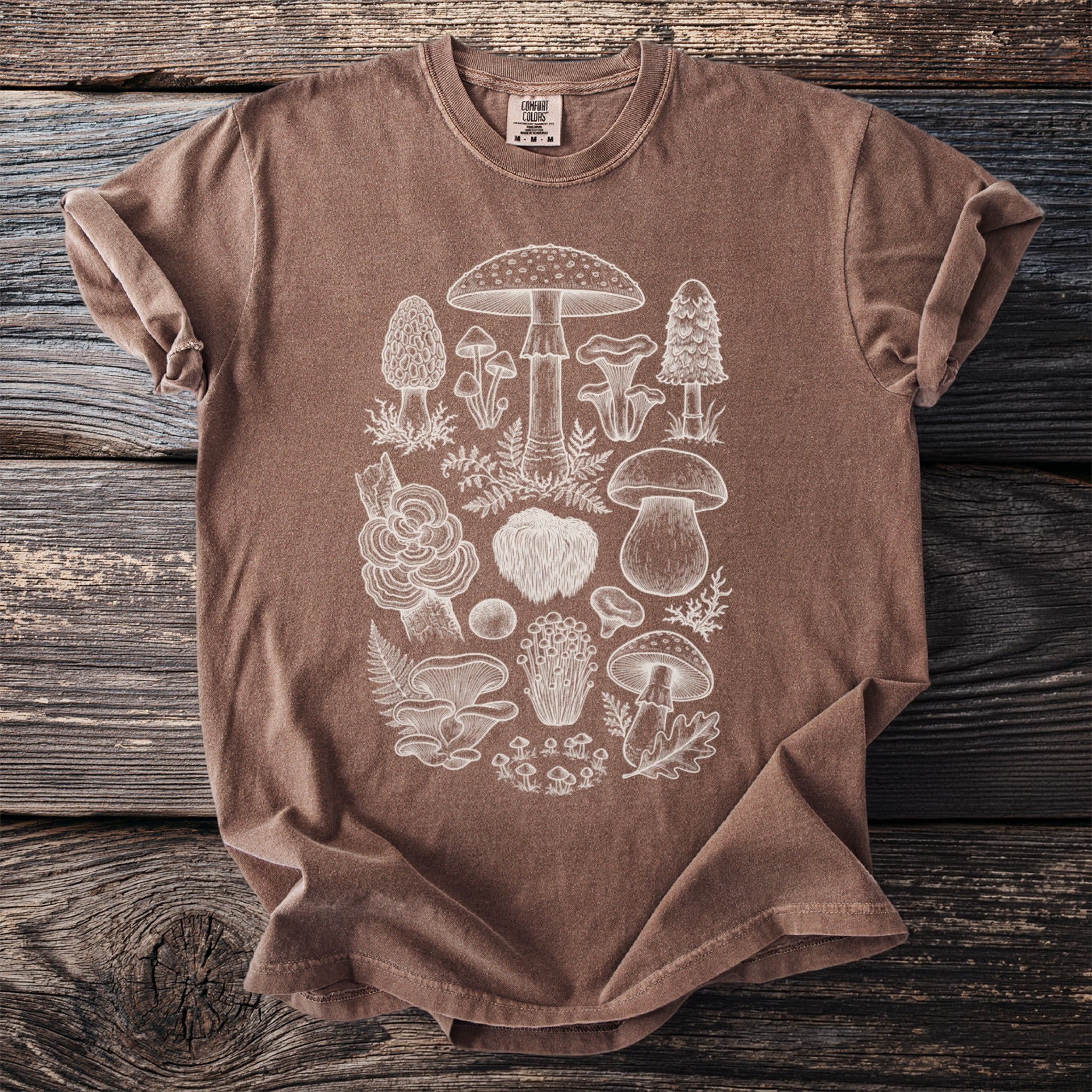 Brown t-shirt with a white line drawing of various mushrooms and ferns.