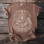 Brown t-shirt with occult graphic of a shaman, raven, wolf, moon phases, and bones.
